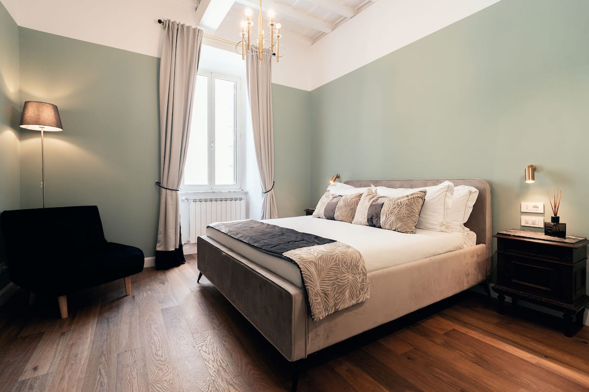 A bedroom with a bed, a chair, a nightstand, and a lamp.