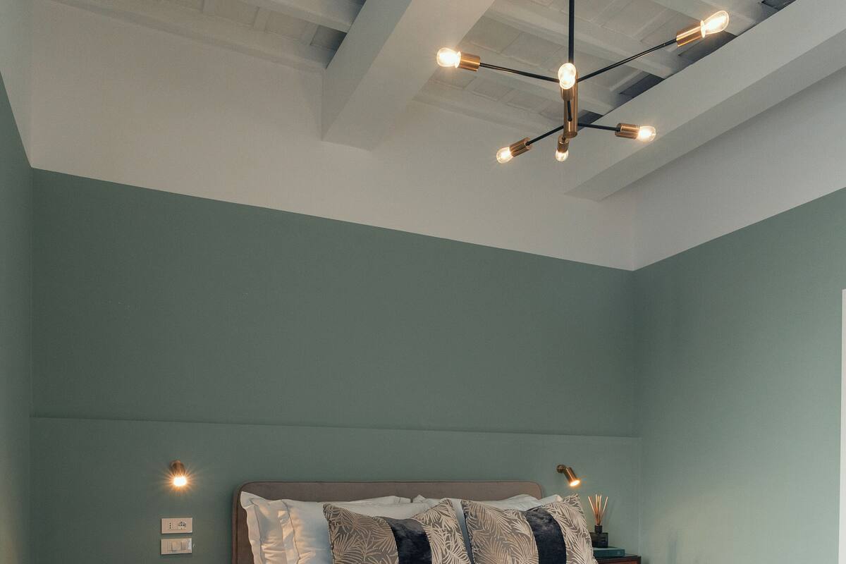 A bedroom with a large bed, wooden flooring, a ceiling light fixture, and a nightstand with a lamp.