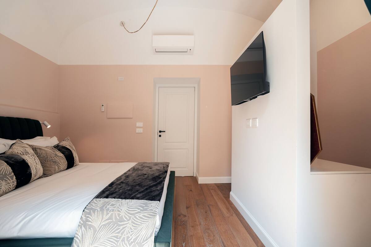 A bedroom with a bed, a door, an air conditioning unit, and a mounted TV.