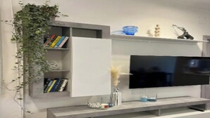 A modern living room with a flat-screen TV mounted on a white wall, a grey built-in bookshelf, and a small decorative shelf with items. - Spacious and Modern Apartment in the Heart of Rome
 (Roma)
