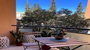 An outdoor balcony with a wooden table, potted plants, and a view of trees and buildings. - Spacious and Modern Apartment in the Heart of Rome
 (Roma)