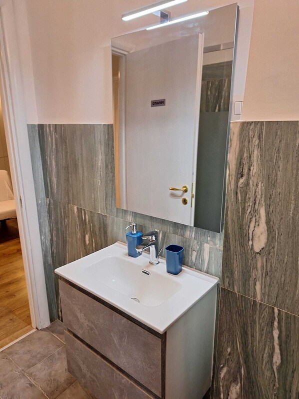 A bathroom with a white sink, blue soap dispenser, and a mirror above it. - "LE VIE DI ROMA" APARTMENT WITH 4 ROOMS AND 12 BEDS, VIA SCIACCA 26, ROME (Roma)