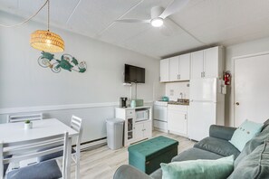 A compact living space with a kitchenette, a dining area, and a seating area with a sofa and ottoman.