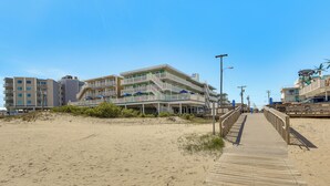 Ein Strandhotel mit mehreren Balkonen, einer Holzpromenade und einem klaren, blauen Himmel.