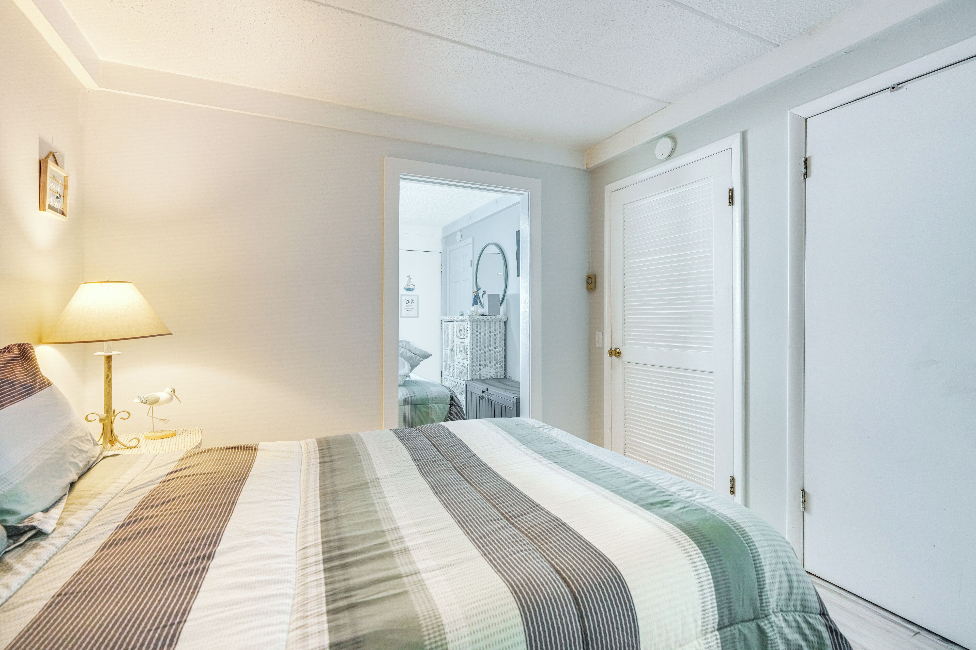 Une chambre à coucher avec un lit, une lampe de chevet, une porte et une vue sur une autre pièce.