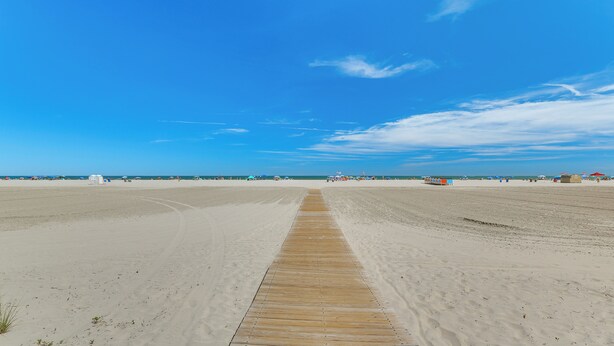 Ein weiter Sandstrand mit einer Holzpromenade, die zum Wasser führt.