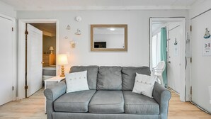 Ein Zimmer mit grauem Sofa, einem spiegelnden Holzrahmen, einer weißen Tür und einem kleinen Tisch mit Lampe.