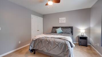 A bedroom with a bed, a ceiling fan, a nightstand with a lamp, and a door.