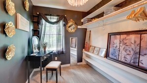 Une pièce avec un mur sombre, un bureau noir avec une chaise, un miroir et une grande œuvre d’art encadrée.
