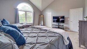 Une chambre avec un grand lit, un ventilateur de plafond, une télévision et une fenêtre avec des rideaux.