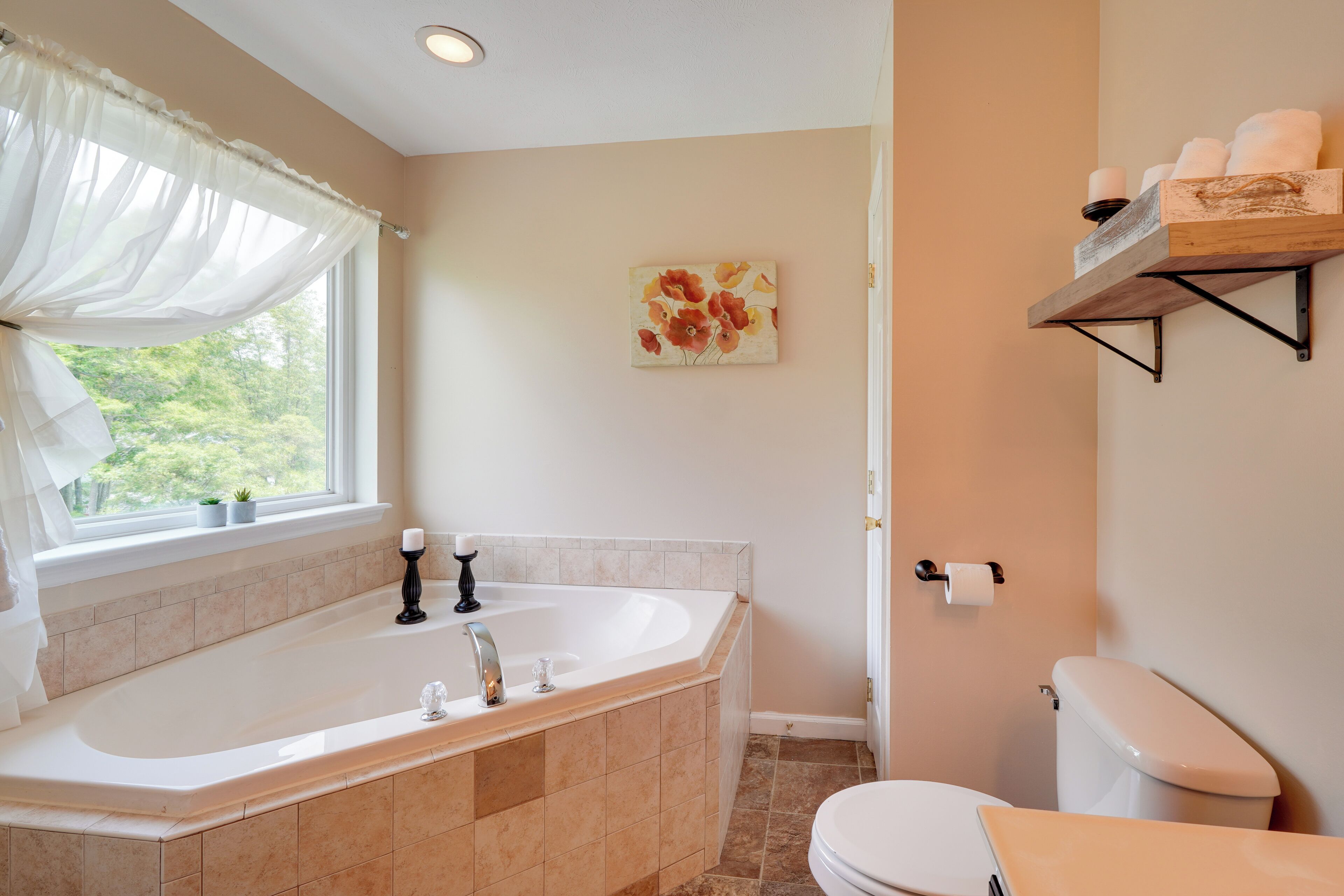 A bathroom with a bathtub, toilet, and a window with a view of trees.
