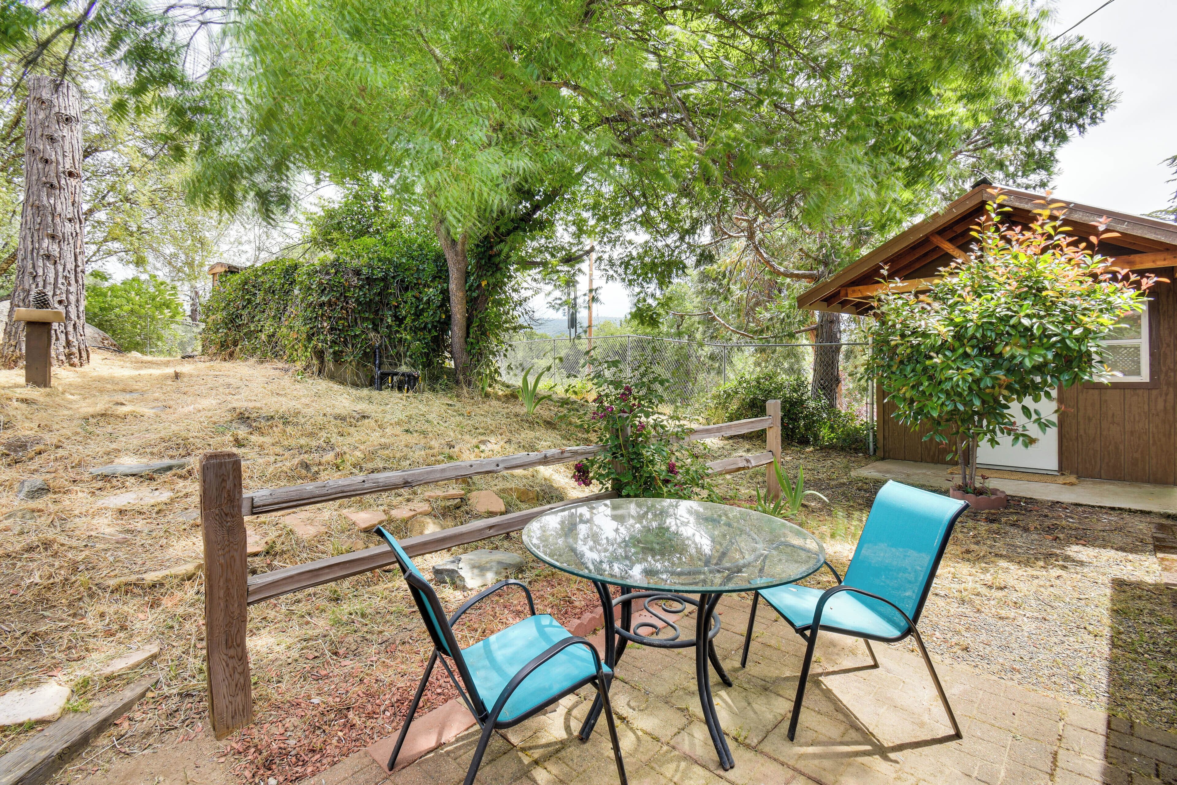 A patio with a glass table and two chairs, surrounded by a wooden fence and trees.