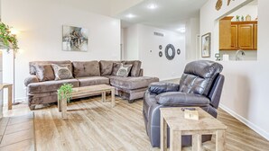 Een moderne woonkamer met een modulaire bank, een leren fauteuil, een houten salontafel en een bijzettafeltje met een plant.