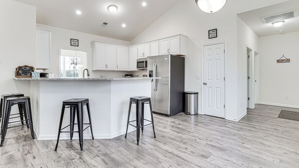 A modern kitchen with white cabinets, a stainless steel refrigerator, and a bar stool. - Savannah Lakes Village Home: Golf & Hike! (McCormick)