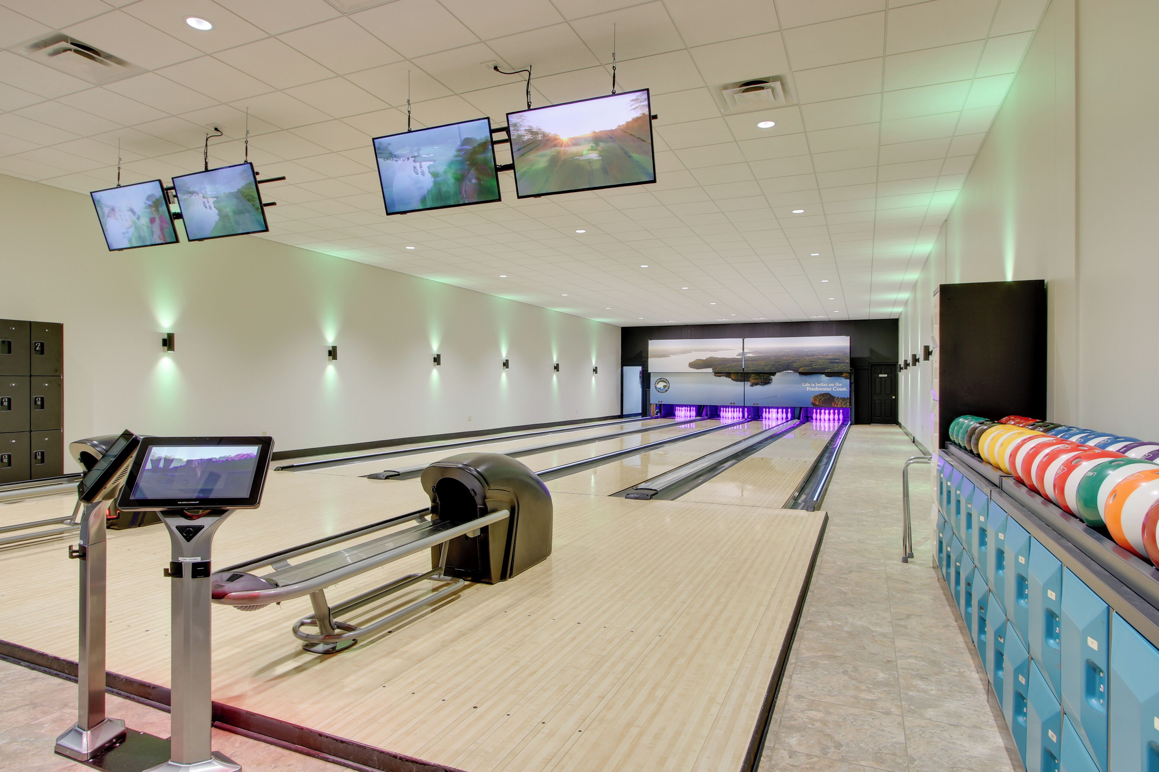 A bowling alley with multiple lanes, overhead monitors, and a row of colorful bowling balls.