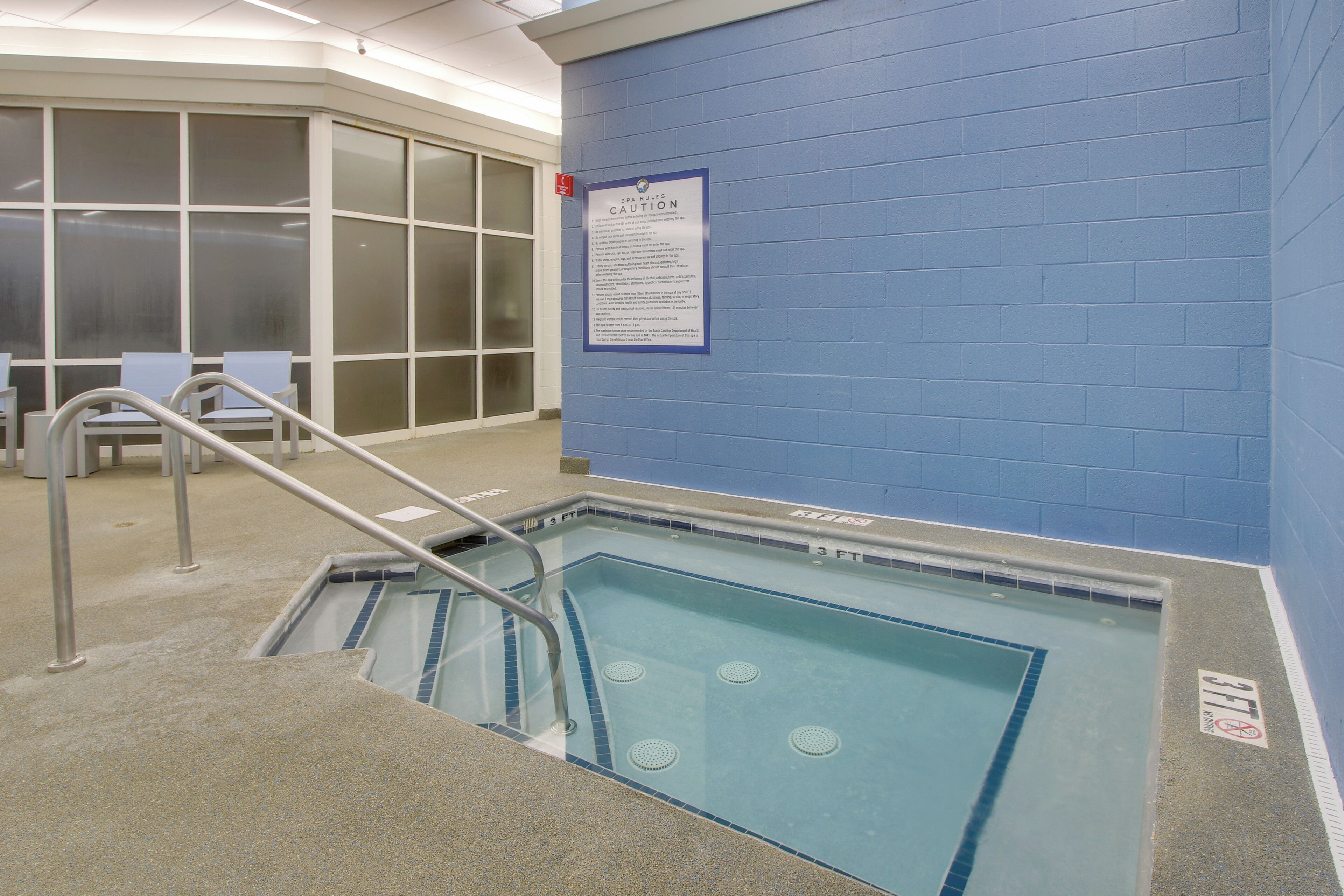 A swimming pool with a caution sign, a glass barrier, and a stairway leading to the pool.