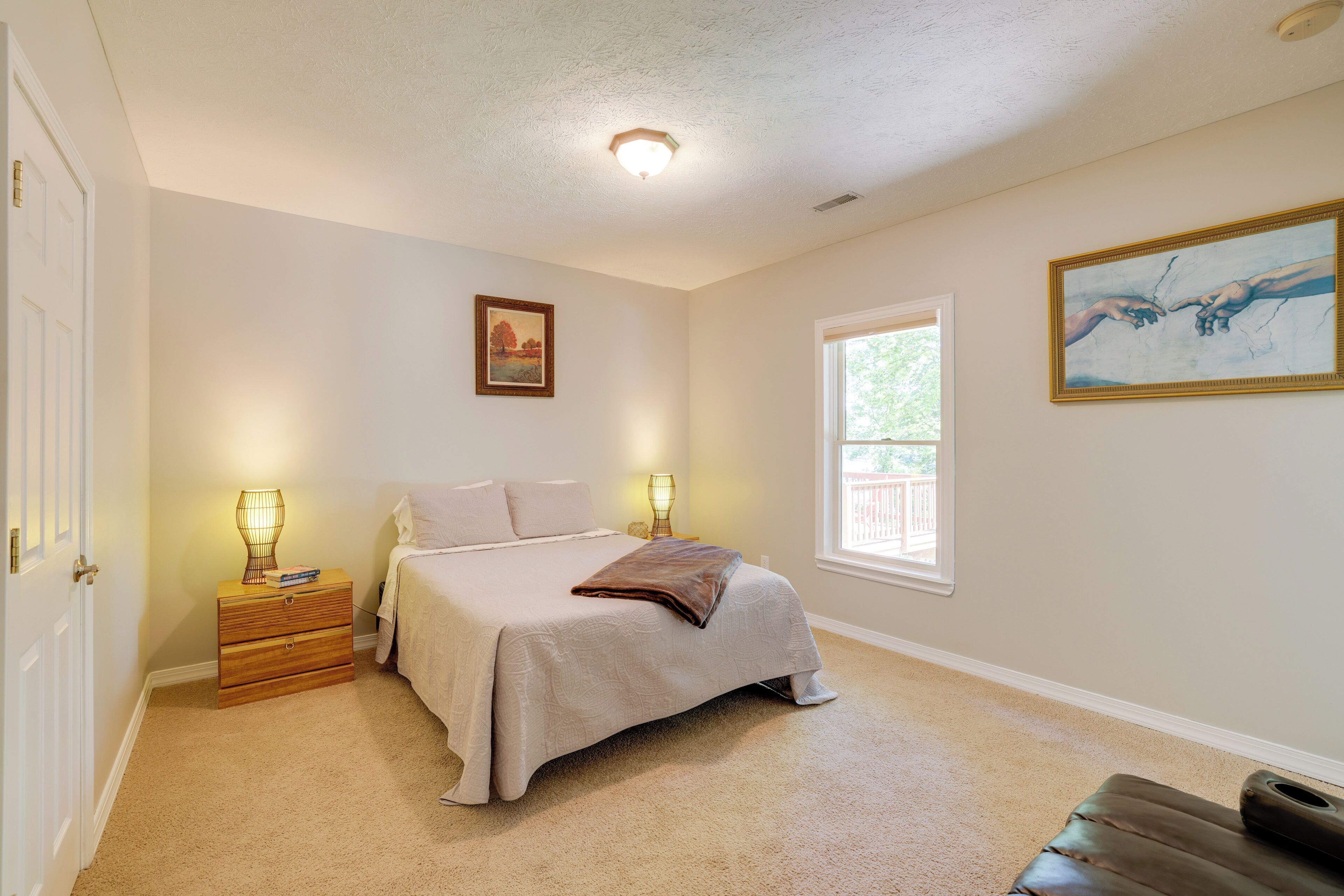 A bedroom with a bed, bedside lamps, a nightstand, a window, and a painting on the wall.