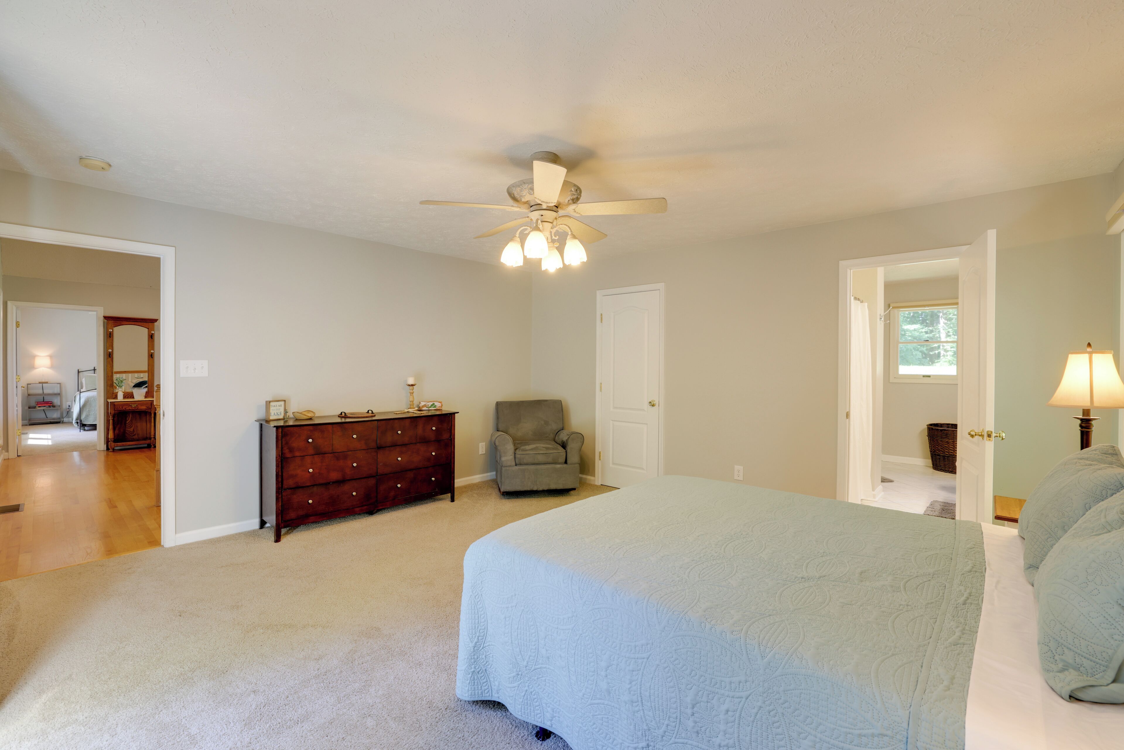 Une chambre avec un grand lit, un ventilateur de plafond, une commode et une chaise.