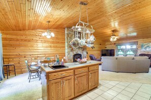 A log cabin interior with a kitchen area featuring wooden cabinets, a stone fireplace, and hanging pots. - 'just a Cast Away' Cassville Cabin w/ Covered Deck (Cassville)