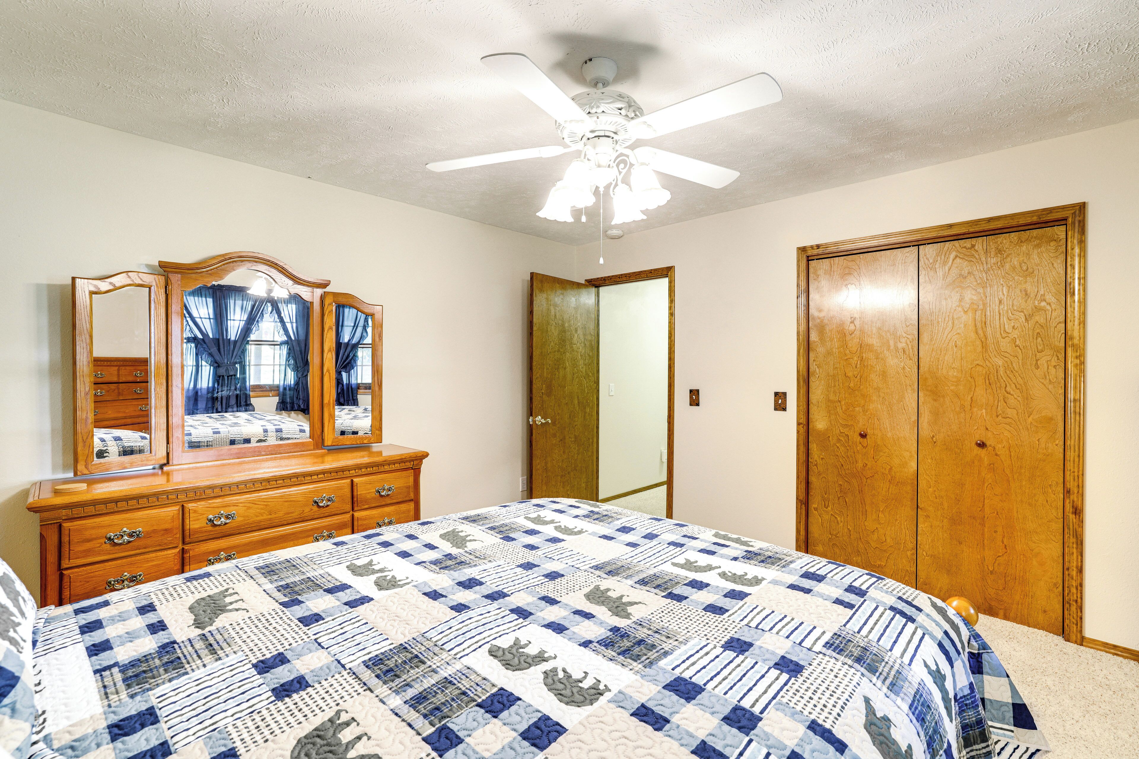 A bedroom with a bed, dresser, mirror, wardrobe, and ceiling fan.