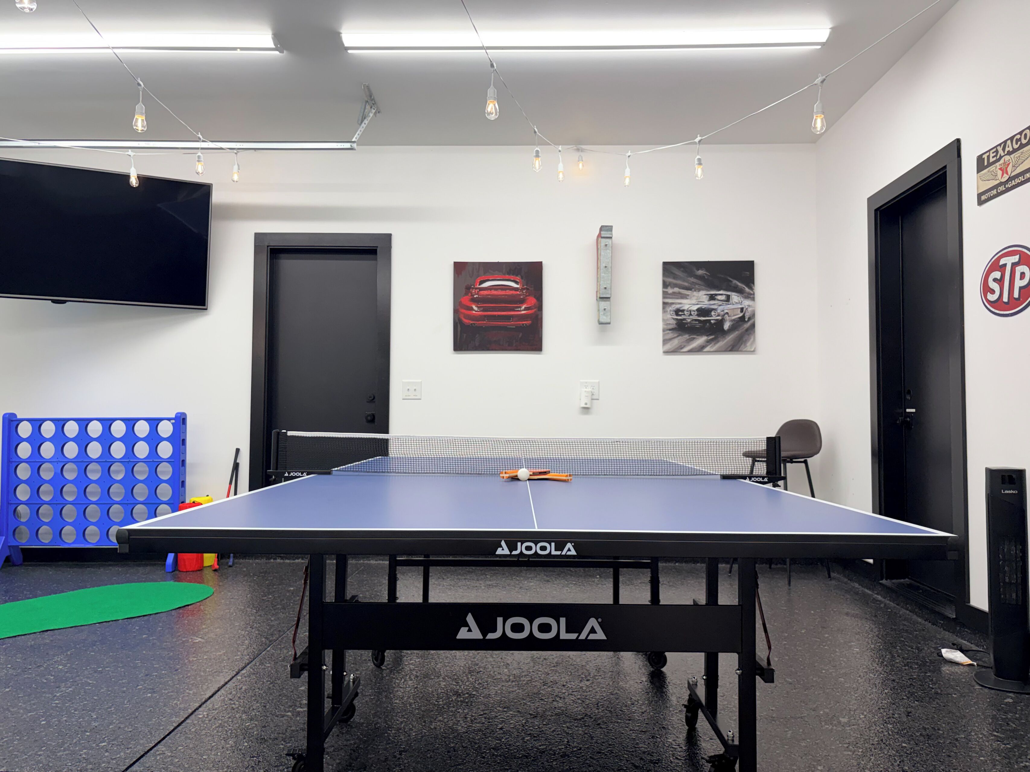 A ping pong table with a net, a blue mat, and a wall-mounted TV.
