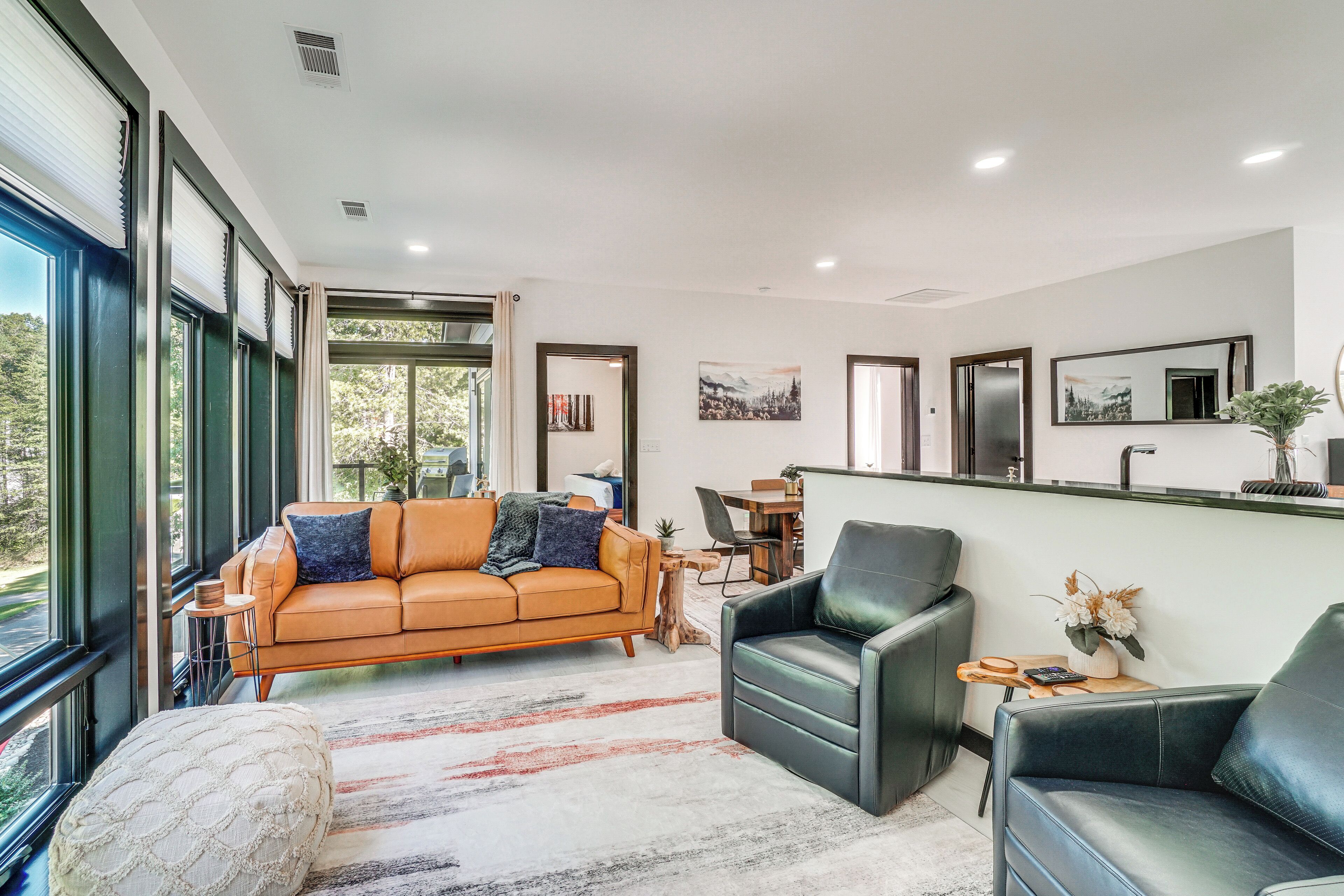 A modern living room with a leather sofa, black armchairs, and a dining area.