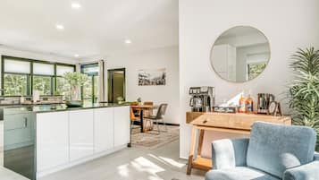 Een moderne keuken met een centraal eiland, een eetgedeelte met een tafel en stoelen, een koffiehoek en een grote spiegel aan de muur.