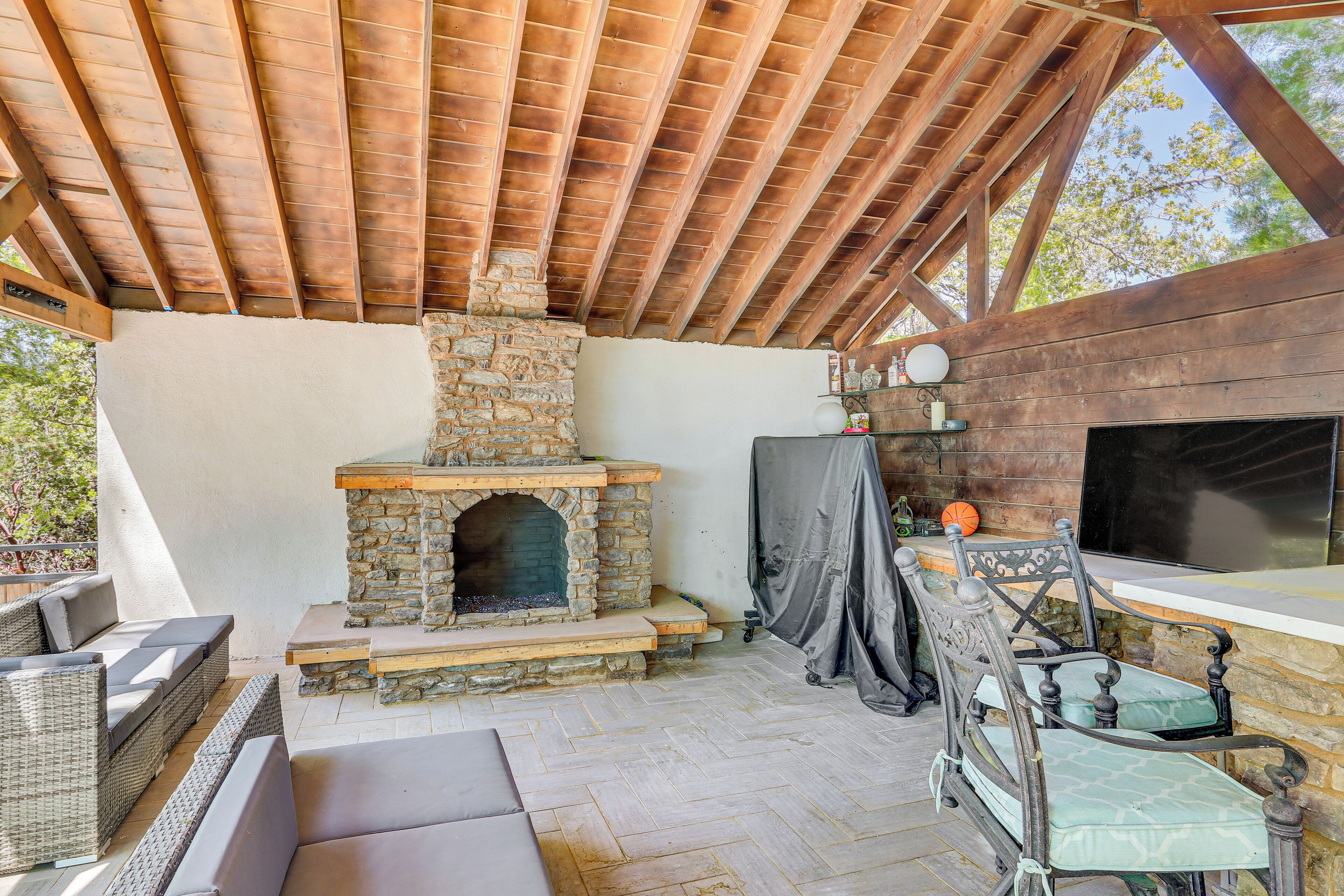 Une terrasse extérieure dotée d’une cheminée en pierre, de meubles en osier et d’une structure de plafond en bois.