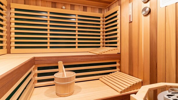 A wooden sauna with benches, a bucket, and two clocks on the wall. - Ferienhaus mit Sauna in St.Peter-Ording (St. Peter-Ording)