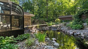 A serene garden with a pond, a wooden deck, and a glass conservatory. - Waterfront Bayview Bliss Bungalow (Brussels)