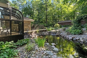 A serene garden with a pond, a wooden deck, and a glass conservatory.