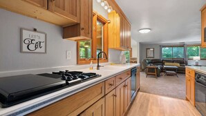 A modern kitchen with wooden cabinets, a gas stove, and a dining area with a leather couch. - Waterfront Bayview Bliss Bungalow (Brussels)