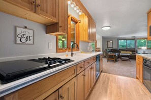A modern kitchen with wooden cabinets, a gas stove, and a dining area with a leather couch.