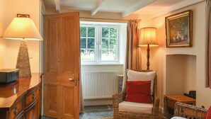 Ein gemütliches Zimmer mit Holztür, Korbmöbeln, einer Heizung und einem Fenster mit Blick auf Grünflächen.