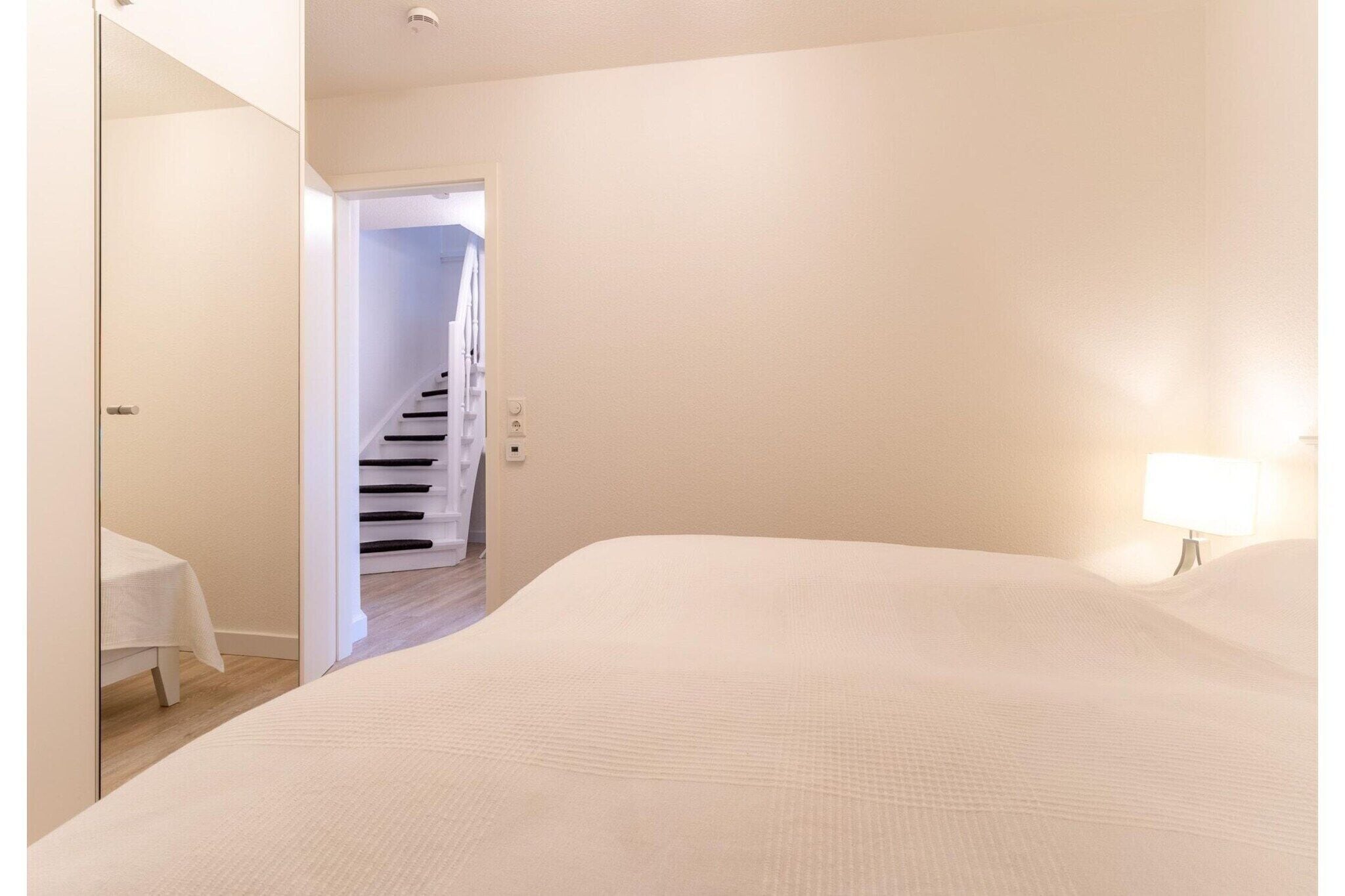 A bedroom with a bed, a nightstand, a lamp, and a door leading to a staircase.