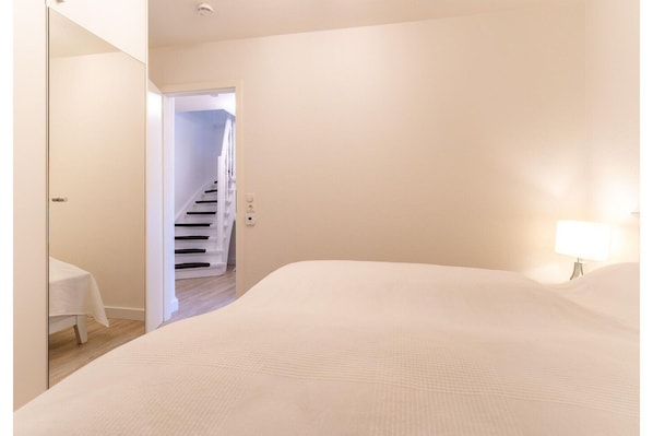 Une chambre à coucher comprenant un lit, une table de chevet, une lampe et une porte donnant sur un escalier.