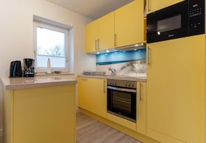 Une cuisine avec des meubles de couleur jaune, un four à micro-ondes, un four traditionnel et une machine à café.
