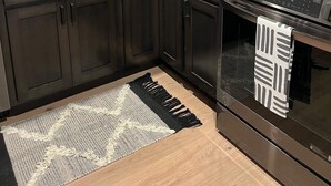 A modern kitchen with dark cabinets, a white tiled backsplash, a stainless steel range hood, and a black and white patterned rug. - DTSF Historic Phillips Loft in the heart of Downtown Sioux Falls (Sioux Falls)