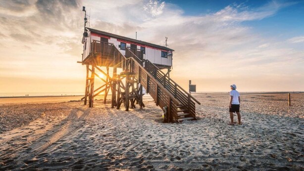 A wooden lifeguard tower on a beach with a person standing nearby. - Ferienwohnung in St. Peter-Ording (St. Peter-Ording)