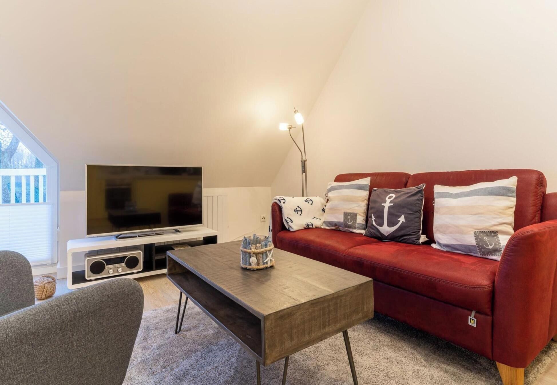 A cozy living room with a red sofa, a wooden coffee table, a flat-screen TV, and a floor lamp.