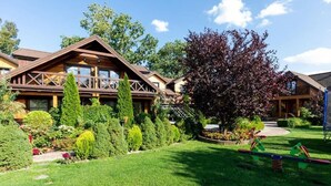 Eine Lodge mit Holzfassade, einem gepflegten Garten und einer Schaukelwippe im Hof.