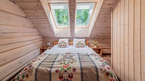 Ein Schlafzimmer mit holzverkleideter Schräge, einem Bett mit Blumenmuster-Bettwäsche, zwei Nachttischen und Dachfenstern.