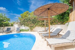 Une piscine entourée de verdure, avec des chaises longues et des parasols, sous un ciel dégagé.