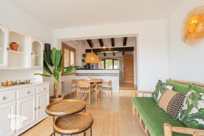 A modern kitchen with white cabinetry, a dining area with wooden chairs, and a green sofa with patterned cushions. - CostaBlancaDreams - Casa Lynn in Javea (Javea / Xàbia)