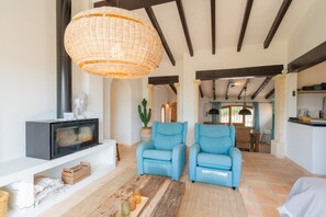 A spacious living area with a fireplace, two blue armchairs, a large woven light fixture, and a rustic wooden coffee table.