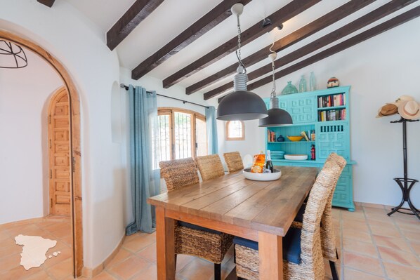 Une table à manger en bois, des chaises en osier, un meuble turquoise rempli de livres et une porte en bois.