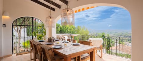 A wooden dining table set with plates, glasses, and a candle, overlooking a scenic view with a balcony and railing.