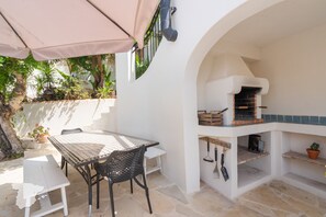 Une terrasse extérieure avec une table et des chaises, un four à pizza et des plantes en pot.