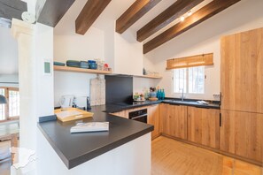 Een moderne keuken met houten kastjes, een zwart aanrecht en een raam met houten zonwering.