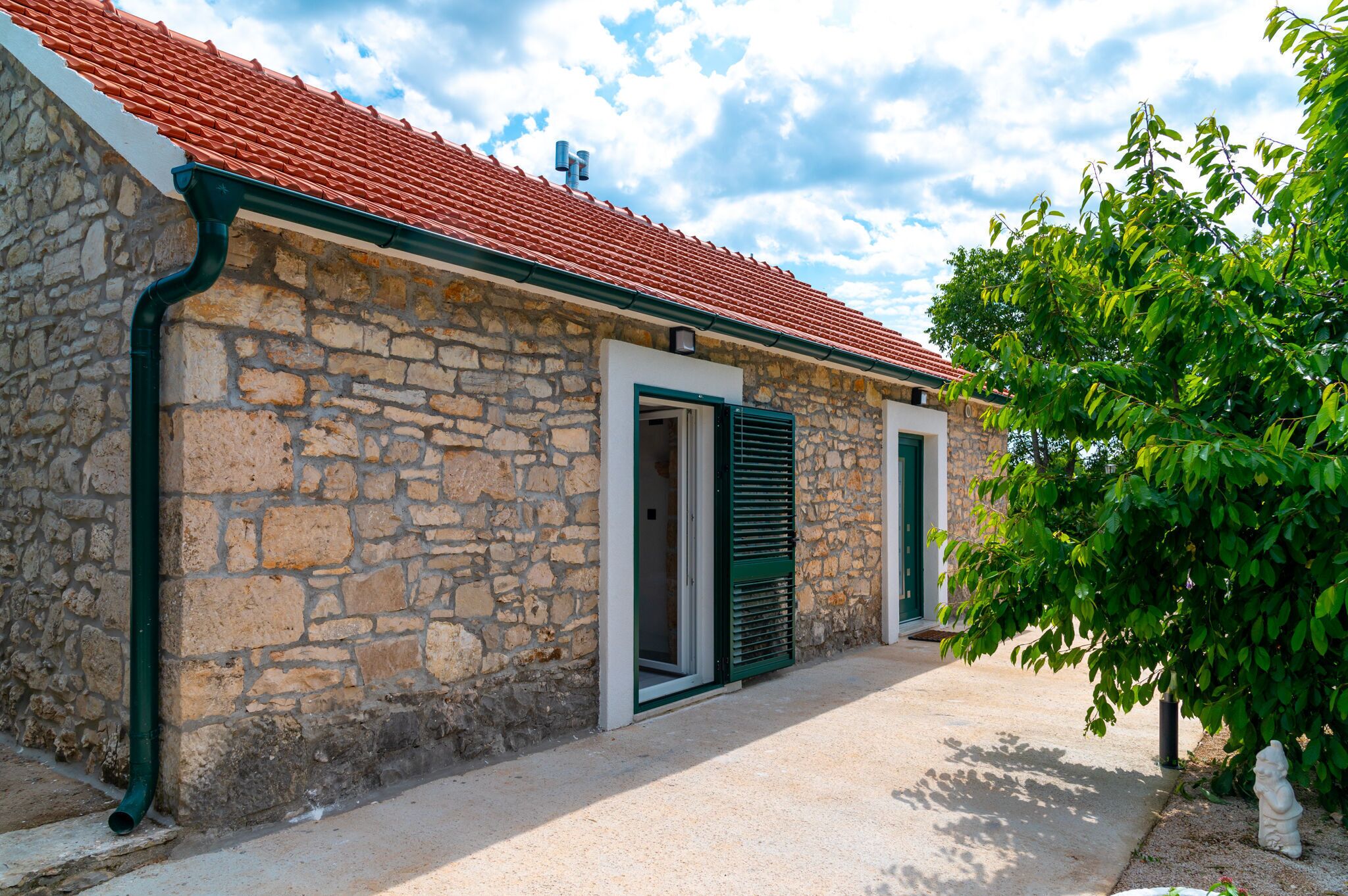 A stone building with a red-tiled roof, a green door, and a small garden area.